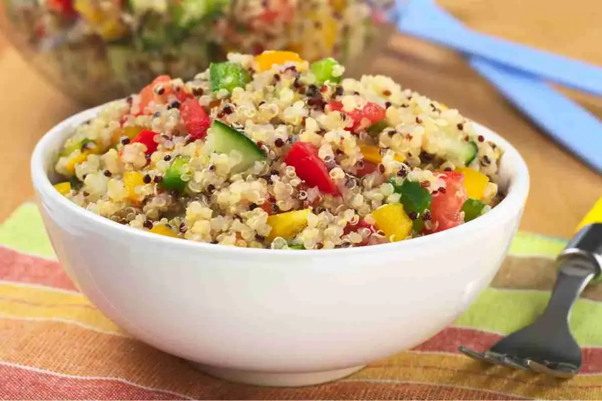 Una ciotola bianca piena di colorata insalata di quinoa con pomodori, cetrioli e peperoni.