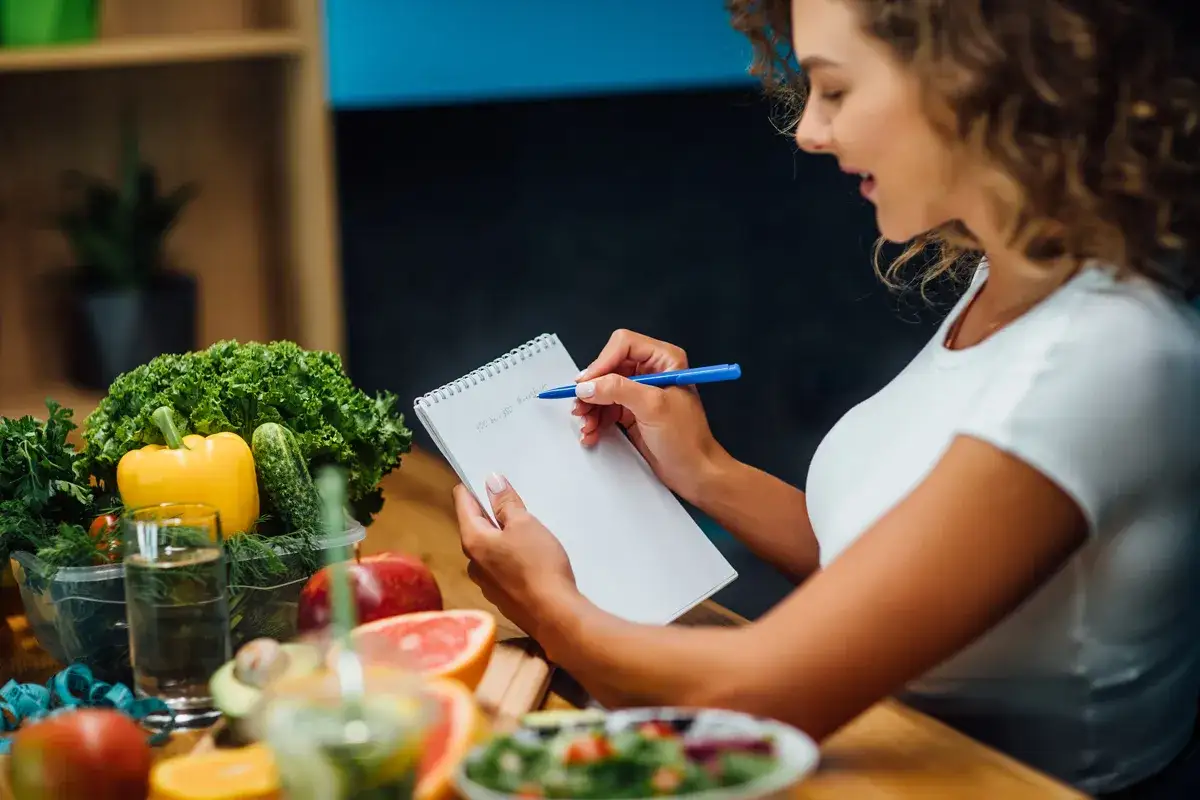 Kobieta planuje dietę na cera naczynkowa, otoczona świeżymi warzywami i owocami.