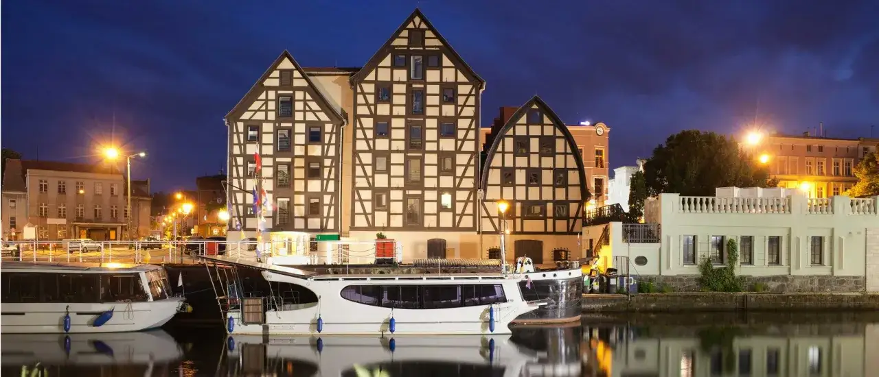 Nocne bydgoszcz atrakcje: zabytkowe kamieniczki nad Brdą, cumujące statki i odbijające się w wodzie światła latarni.