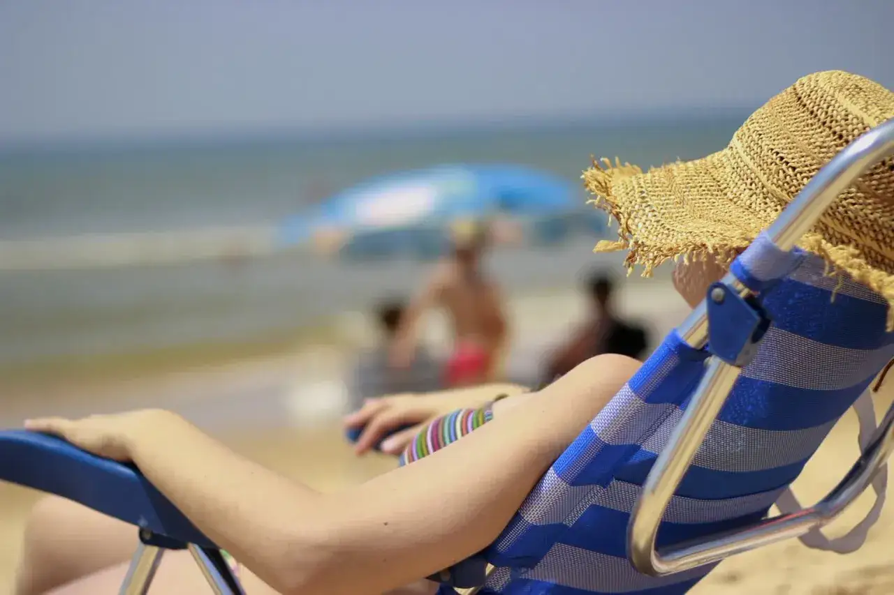 Osoba w słomkowym kapeluszu odpoczywa na plaży. Może to być moment relaksu po otrzymaniu odszkodowania od biura podróży.