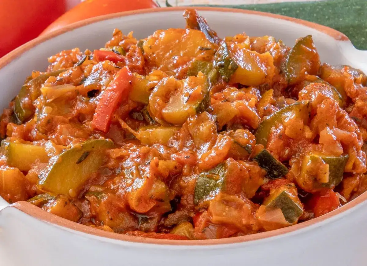Pyszny bigos z cukinii, pomidorów i papryki w sosie pomidorowym, podany w białej misce.
