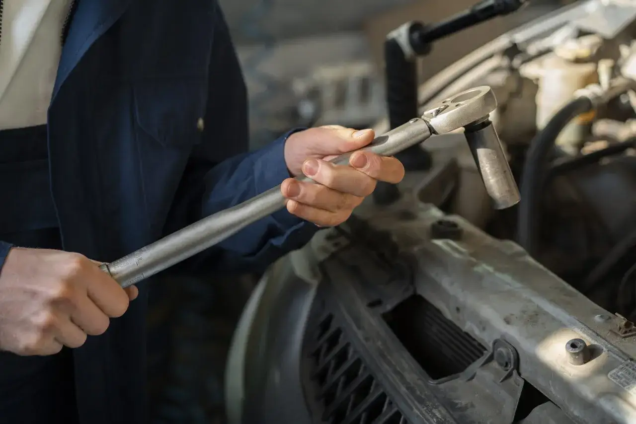 Mechanik z kluczem nasadowym przy silniku. Czy mechanik może żądać dopłaty za utylizację starego akumulatora bez Twojej zgody?