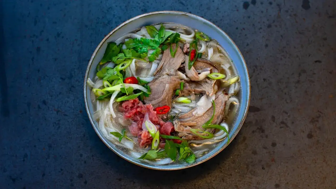 Eine dampfende Sch&uuml;ssel Pho Suppe mit zarten Rindfleischscheiben, Reisnudeln, frischen Kr&auml;utern und Chili.
