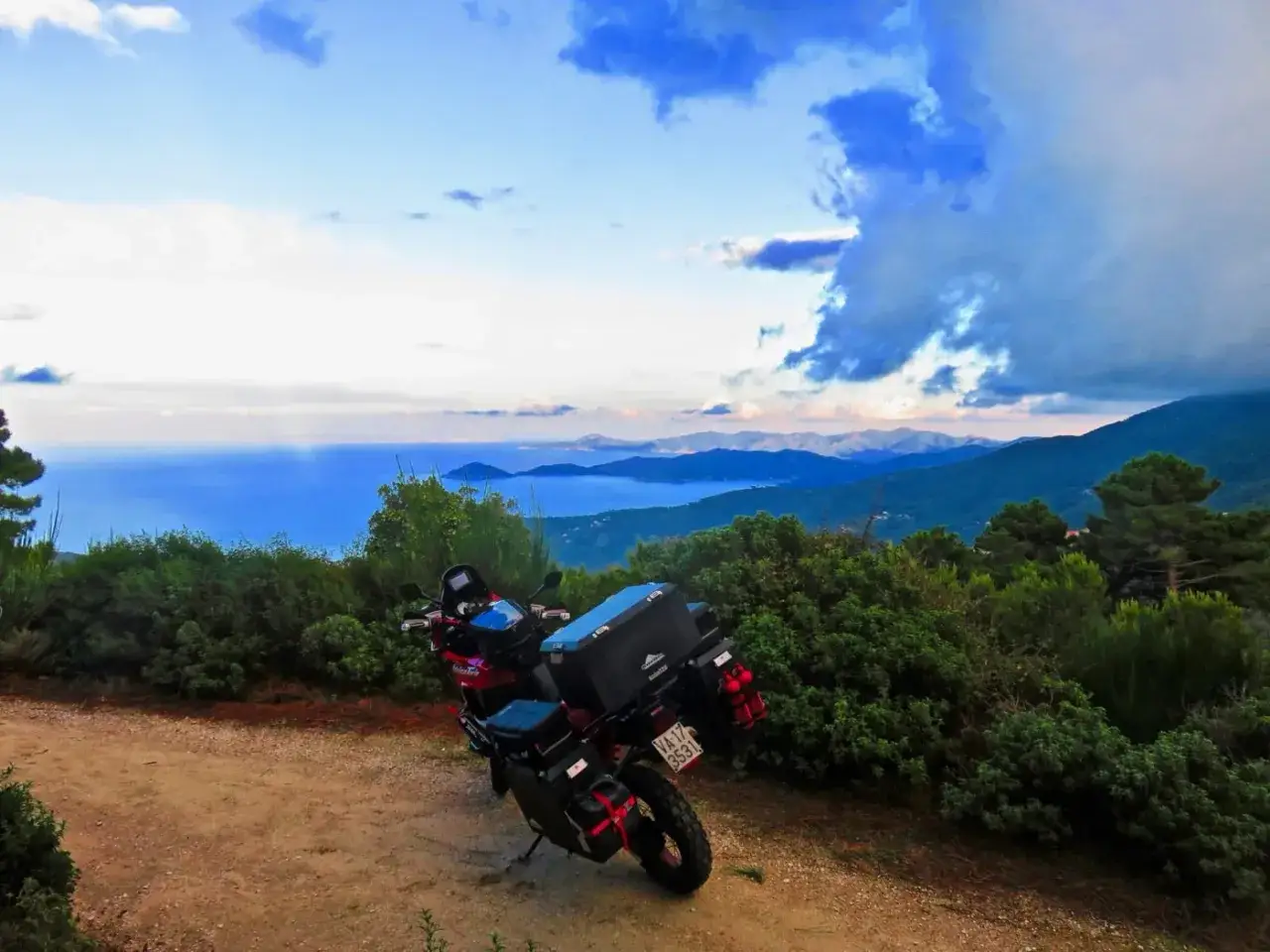 Moto pronta per l'avventura a Elba. Vista mozzafiato sul mare e sulle colline verdi, con nuvole drammatiche nel cielo.