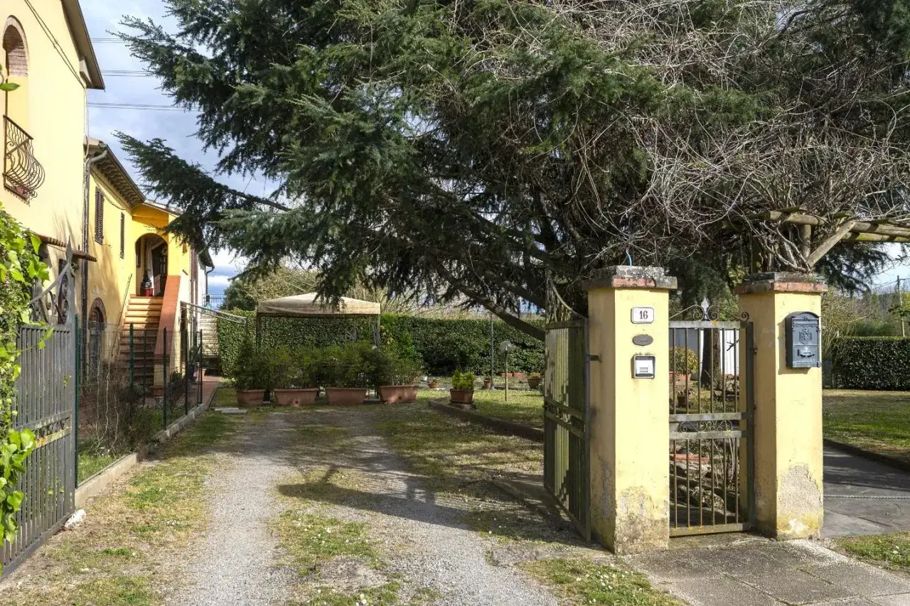 Ingresso di una cascina in un paese tranquillo, con cancello in ferro battuto e un grande albero.