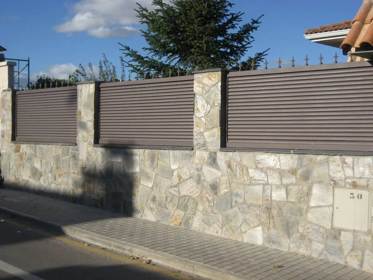 Muro de piedra con lamas horizontales, un ejemplo de tipos de vallas para chalet que combinan estética y privacidad.