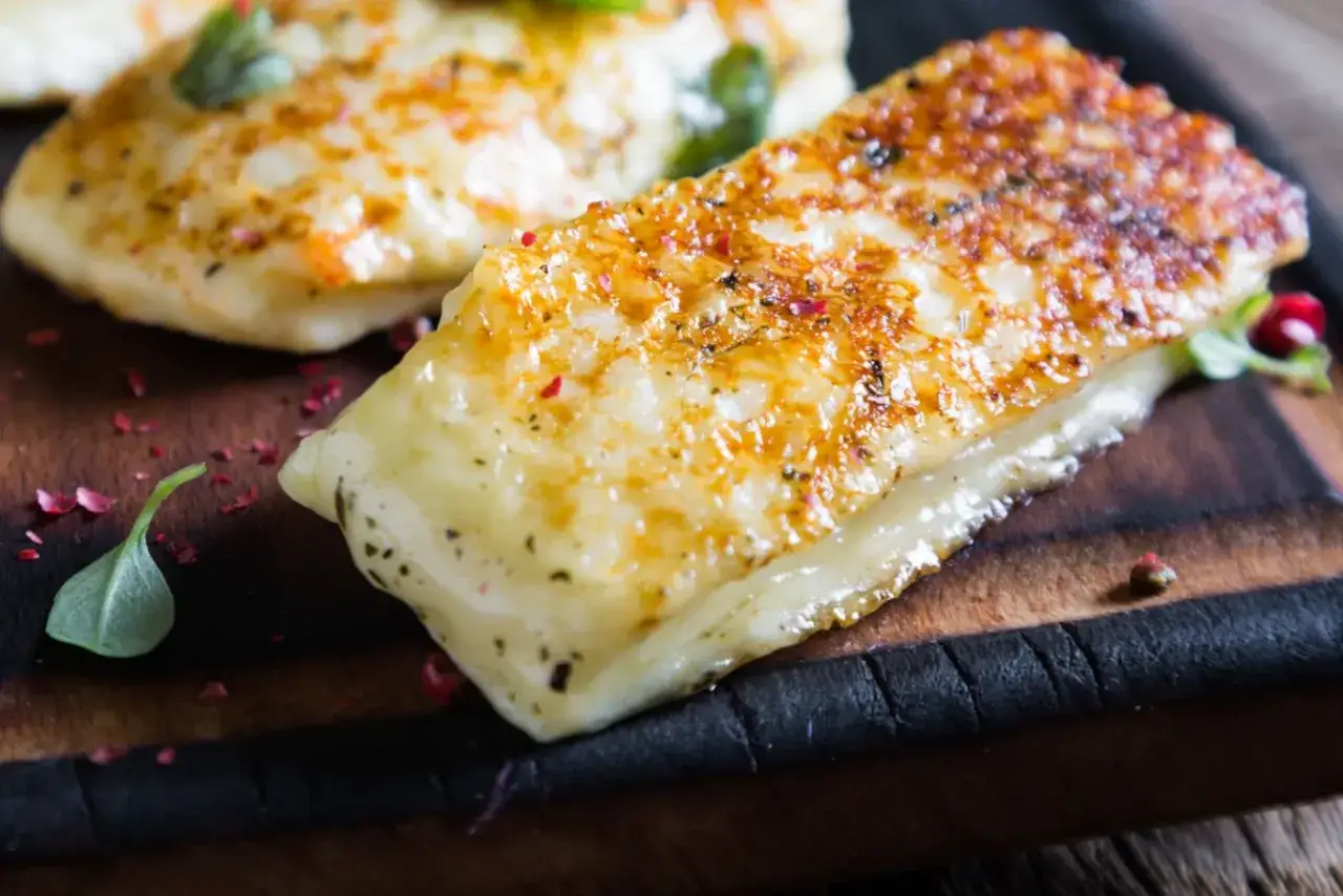 Złociste halloumi z grilla, posypane pieprzem i ziołami, podane na drewnianej desce.