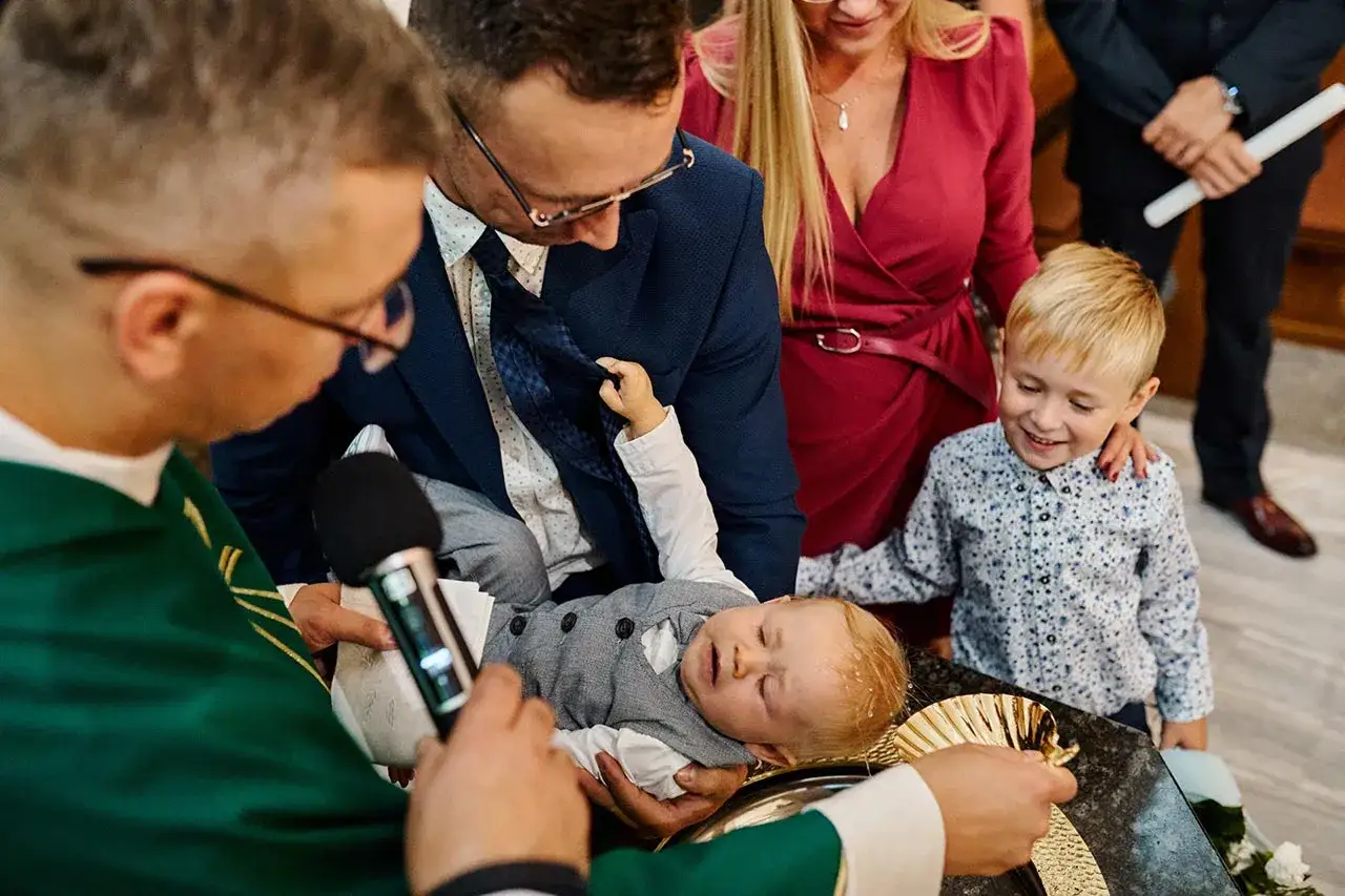Chrzest dziecka. Rodzice trzymają malucha, ksiądz udziela sakramentu. Warto wiedzieć, ile kosztuje fotograf na chrzest, by uwiecznić te chwile.