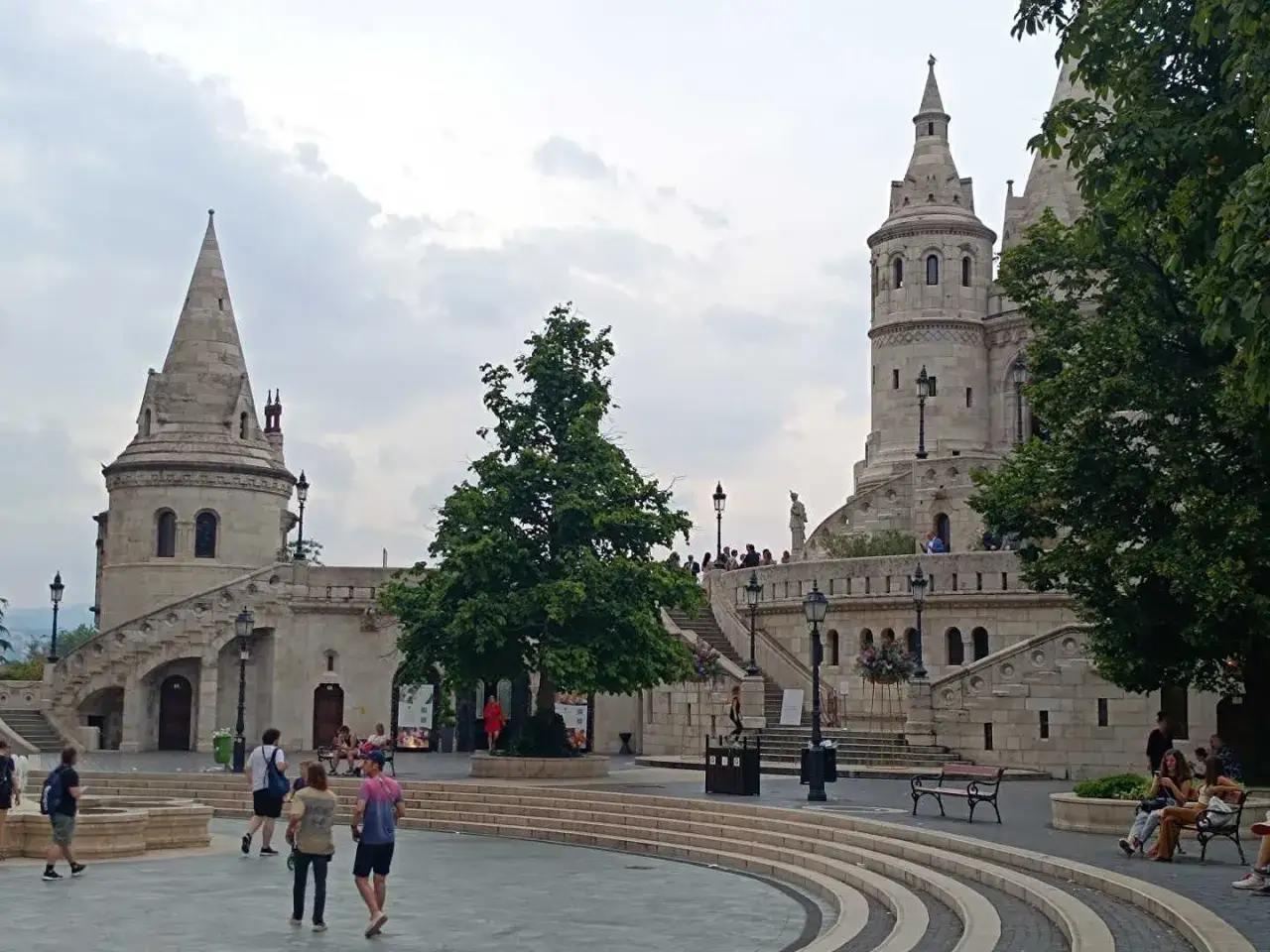 Budapeszt: Rybacka Baszta, kamienne wieże i schody, plac z drzewem i spacerującymi ludźmi. Jedna z głównych atrakcji w Budapeszcie.