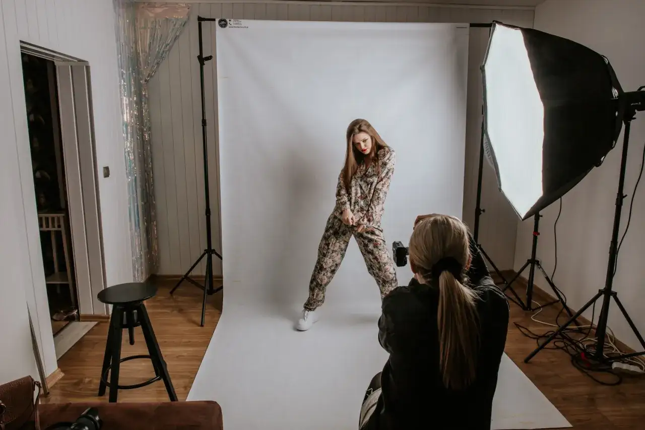 Sesja fotograficzna mody: modelka w kwiecistym kombinezonie pozuje do zdjęcia, fotografka z aparatem w ręku.