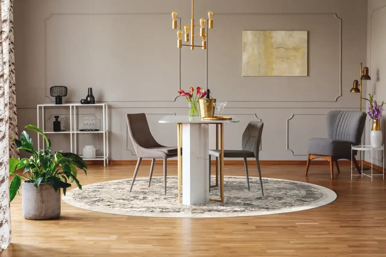 En rund matta under ett elegant runt matbord med tv&aring; stolar. En guldig taklampa lyser upp rummet.