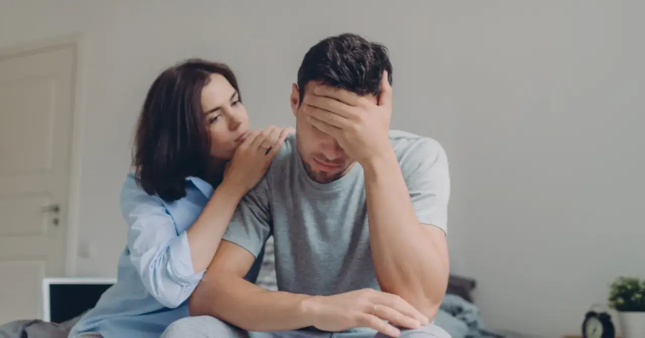 Kobieta pociesza zmartwionego mężczyznę, gdy facet wzdycha przy kobiecie. Jej dłoń spoczywa na jego ramieniu, oferując wsparcie.