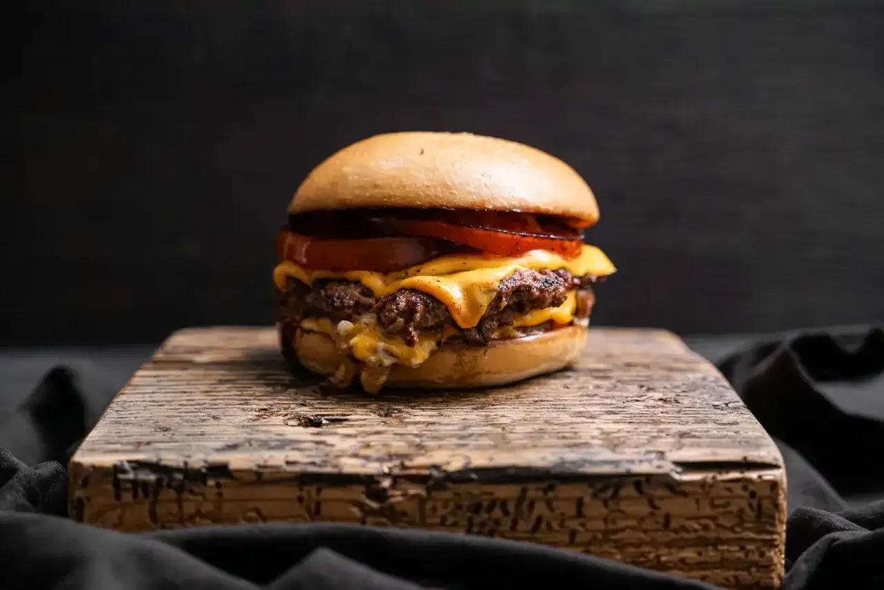 Saftiger Oklahoma Smash Burger mit geschmolzenem Käse und Tomaten auf rustikalem Holzbrett.