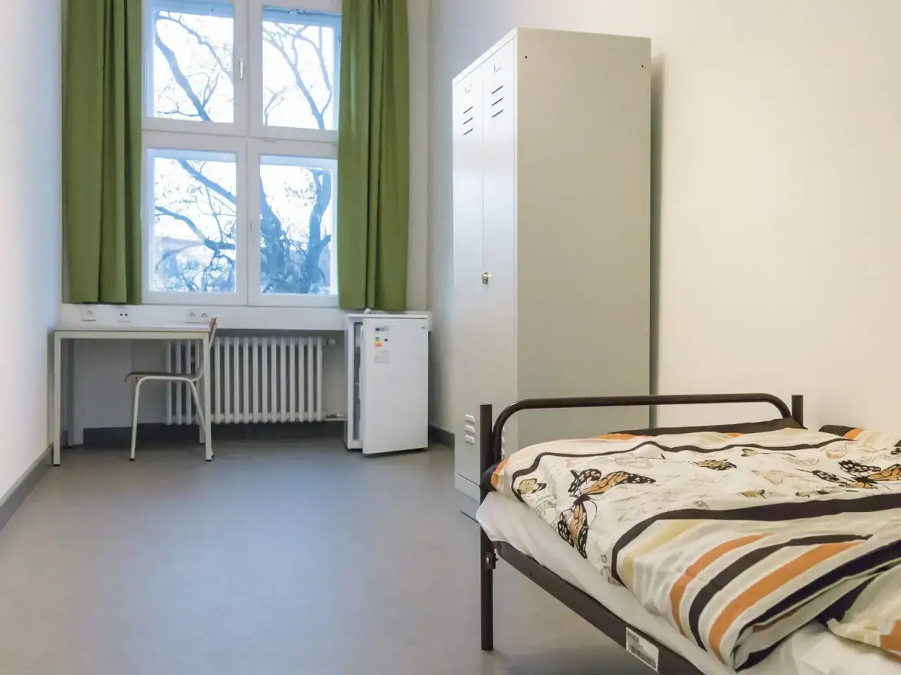 Ein einfaches Zimmer mit Bett, Schrank, Schreibtisch und Kühlschrank. Ein Ort, wohin ohne Geld und Wohnung?