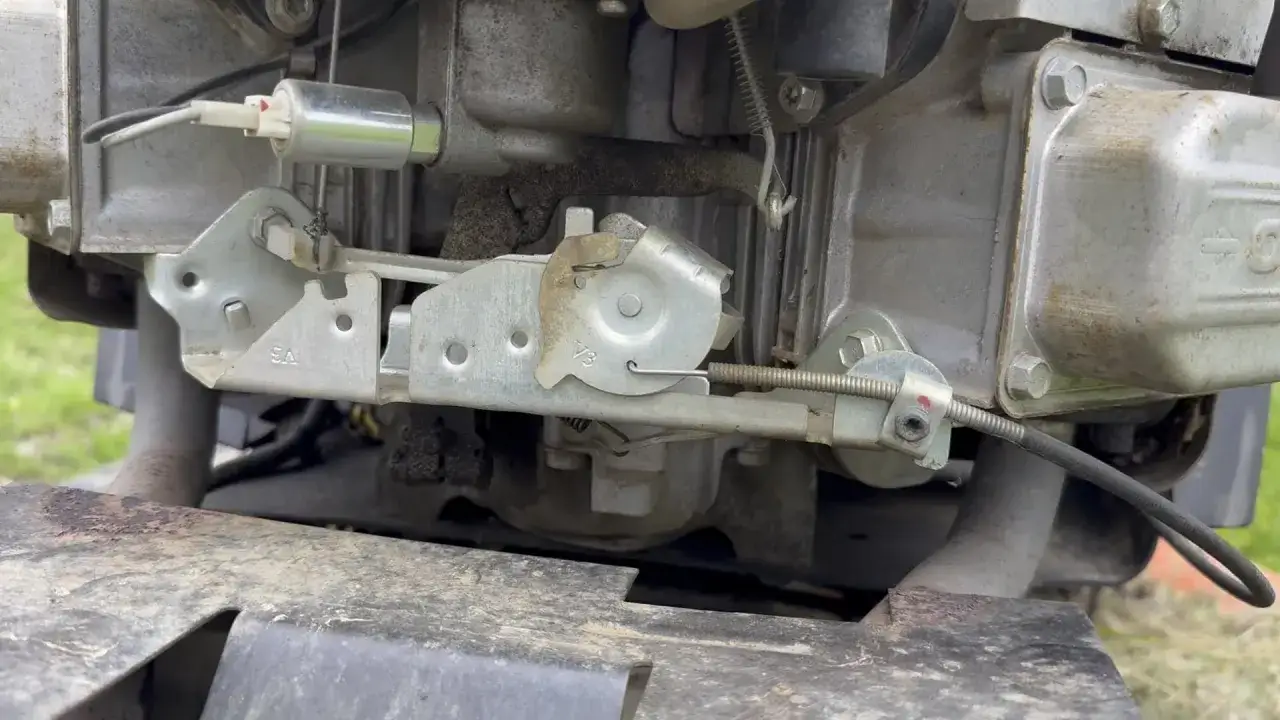 Mechanizm gazu w kosiarce, który sprawia, że kosiarka odpala i gaśnie. Widoczny jest element mocowania linki gazu i sprężyna.