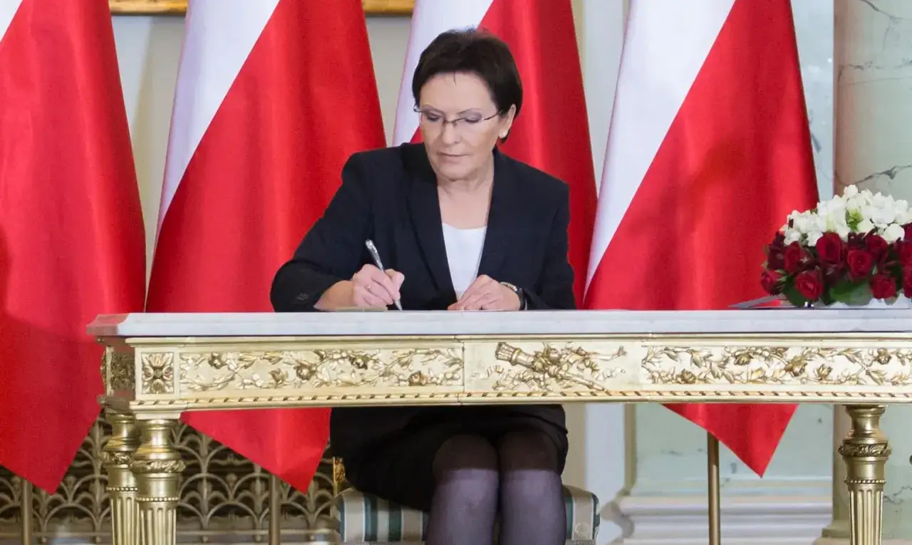 Ewa Kopacz podpisuje dokumenty na tle flag. Czy dostała się do Sejmu? Tak, jej mandat jest ważny.