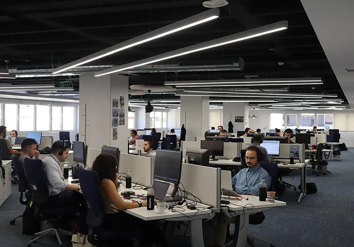 Oficina moderna con empleados trabajando en sus ordenadores. Un joven disfruta de su **spain internship** en este entorno colaborativo.