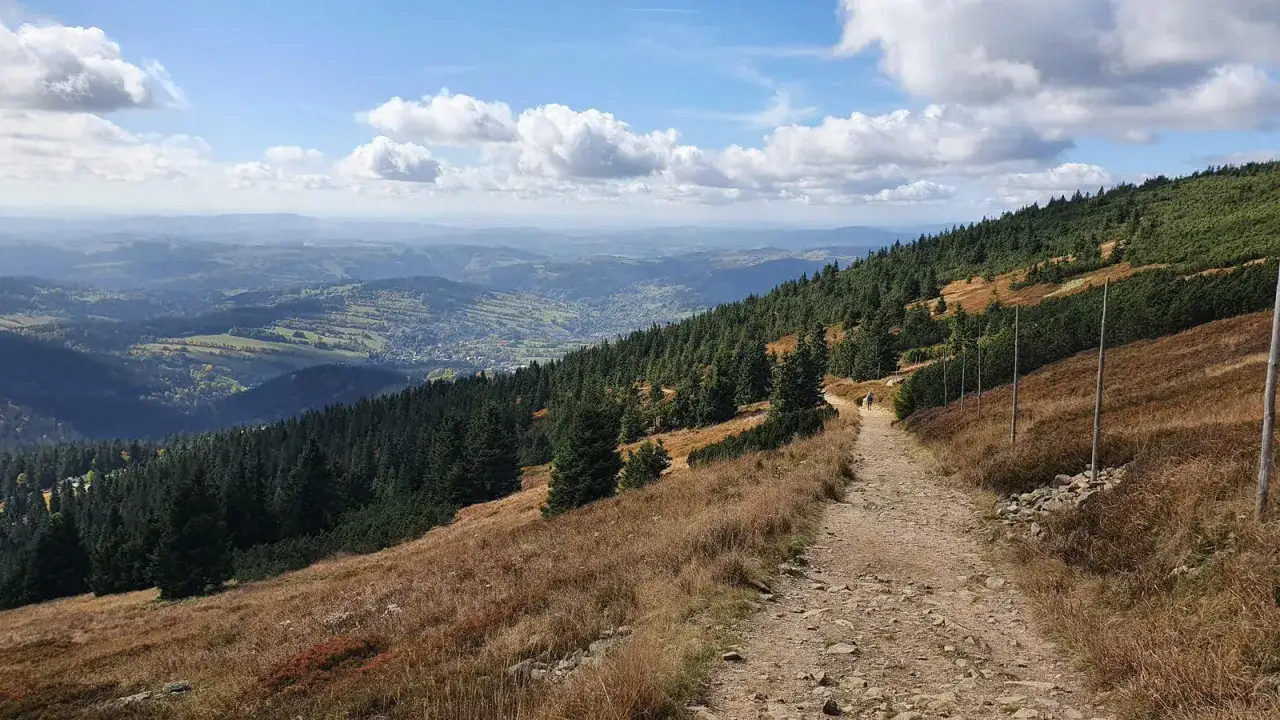 Ścieżka w g&oacute;rach prowadzi w stronę doliny z widokiem na Harrachov. W oddali majaczy wodospad Panczawy.