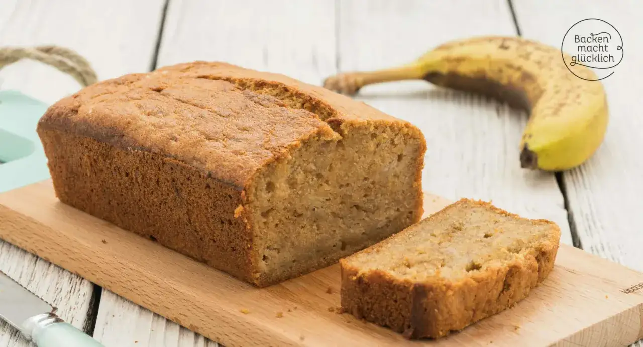 Saftiges Bananenbrot mit Dinkelmehl, eine Scheibe abgetrennt, daneben eine Banane. Backen macht gl&uuml;cklich!