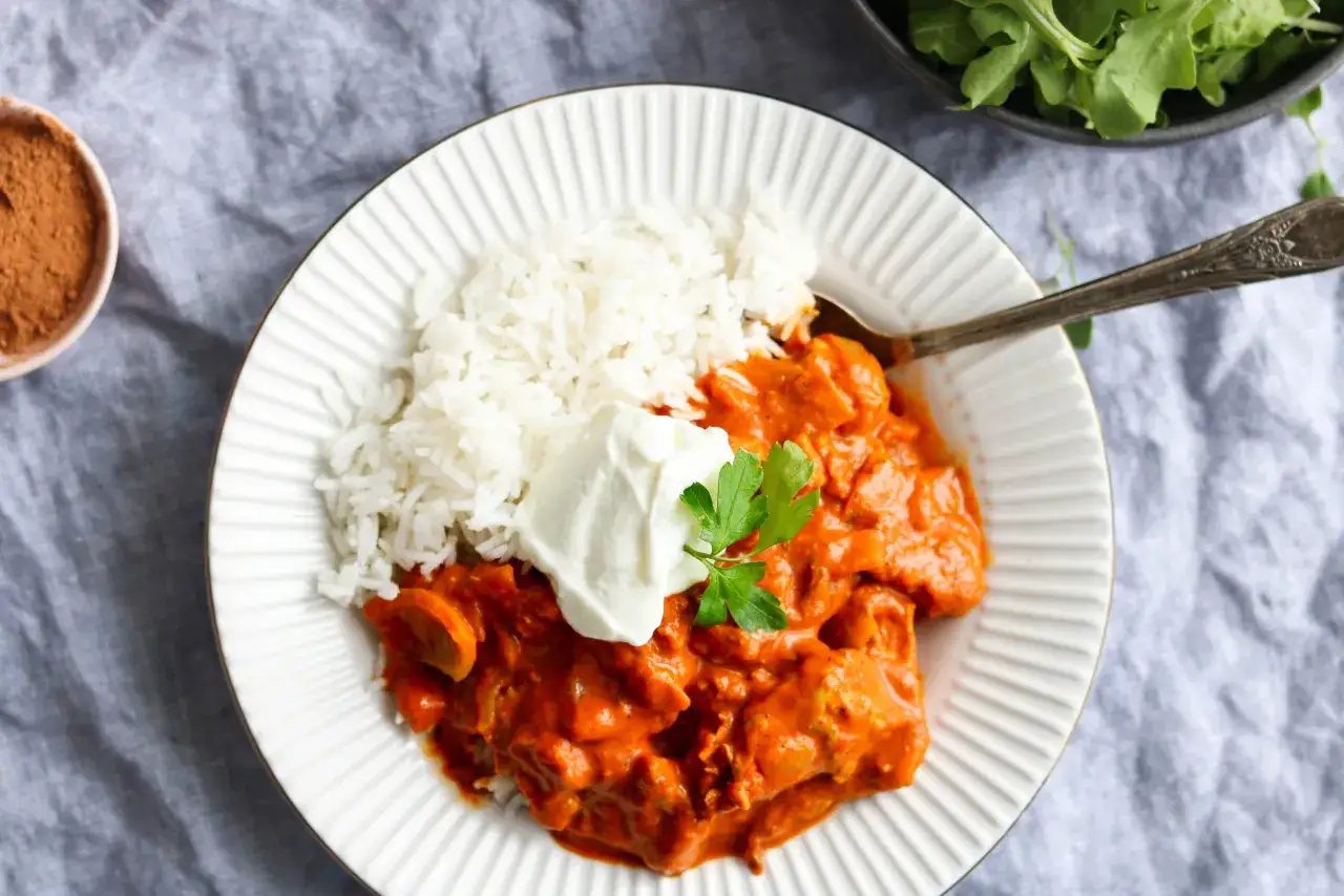 Une assiette de riz blanc avec un poulet au curry cr&eacute;meux et une touche de persil. Une cuill&egrave;re est pos&eacute;e sur le plat.