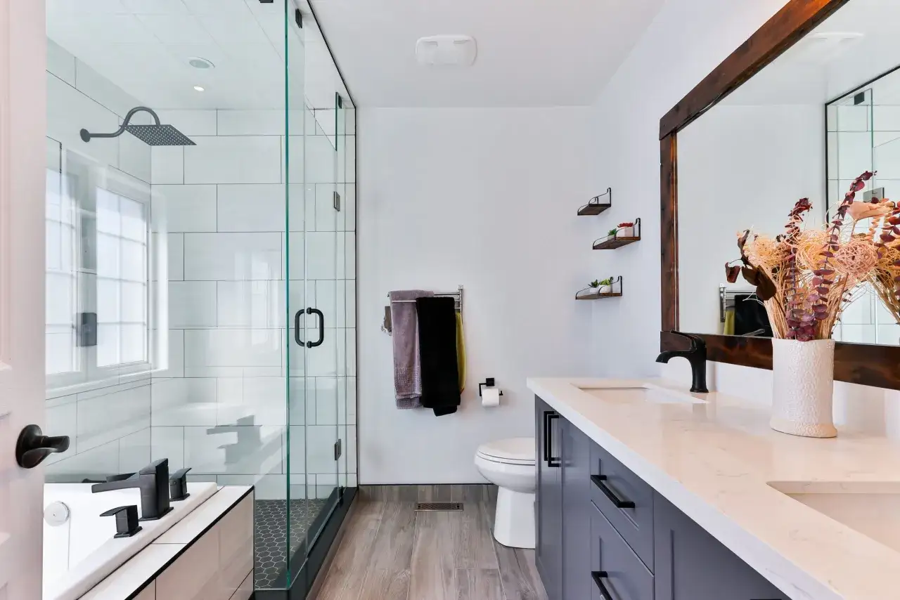 Moderno baño con ducha de cristal y ventana, tocador doble, inodoro y bañera.