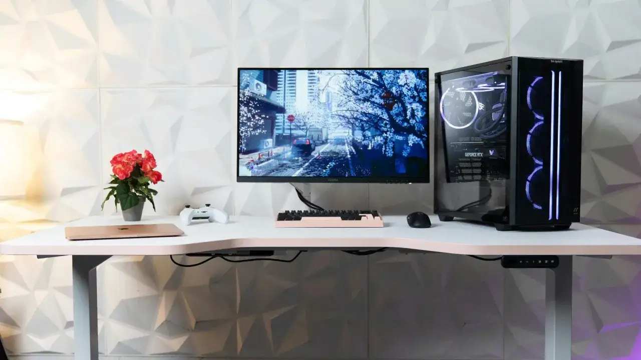 Bureau moderne avec écran, tour PC lumineuse, clavier rose, souris, manette et plante. Le branchement PC est soigné sous le bureau.