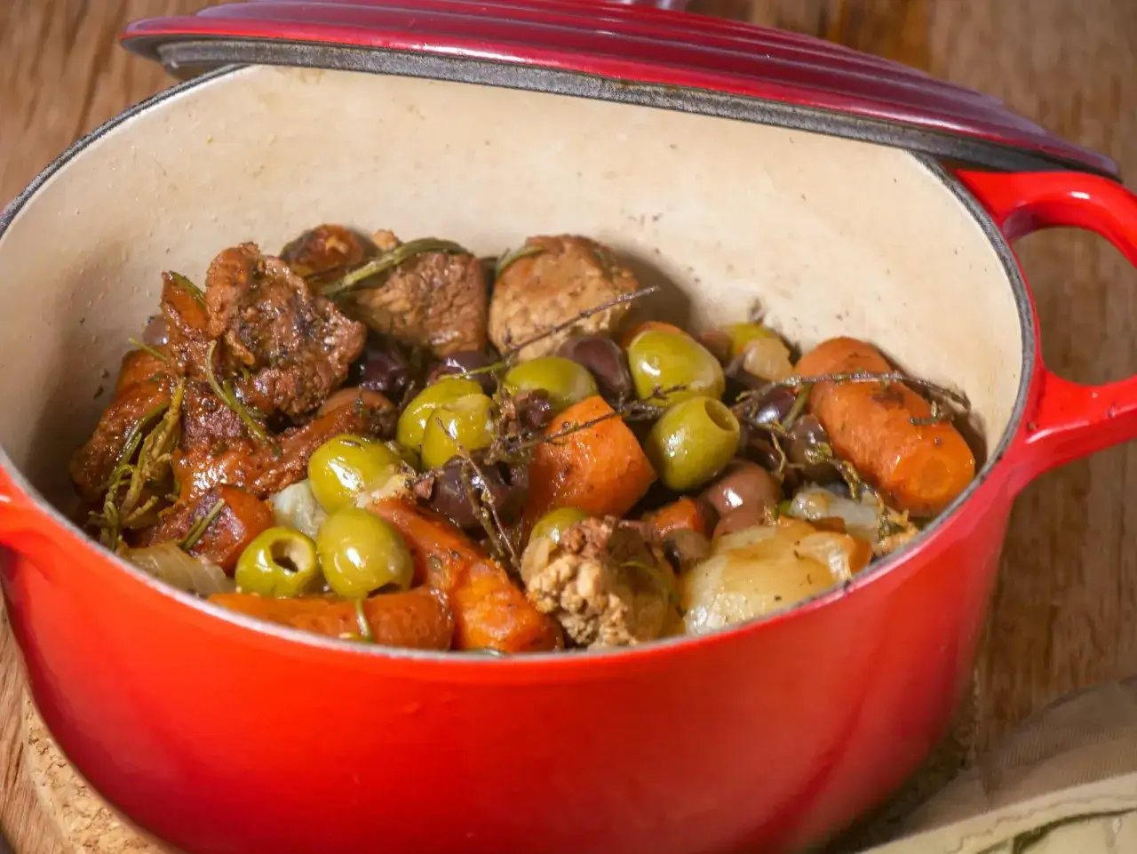 Un savoureux sauté de veau aux olives, carottes et herbes aromatiques mijote dans une cocotte rouge.