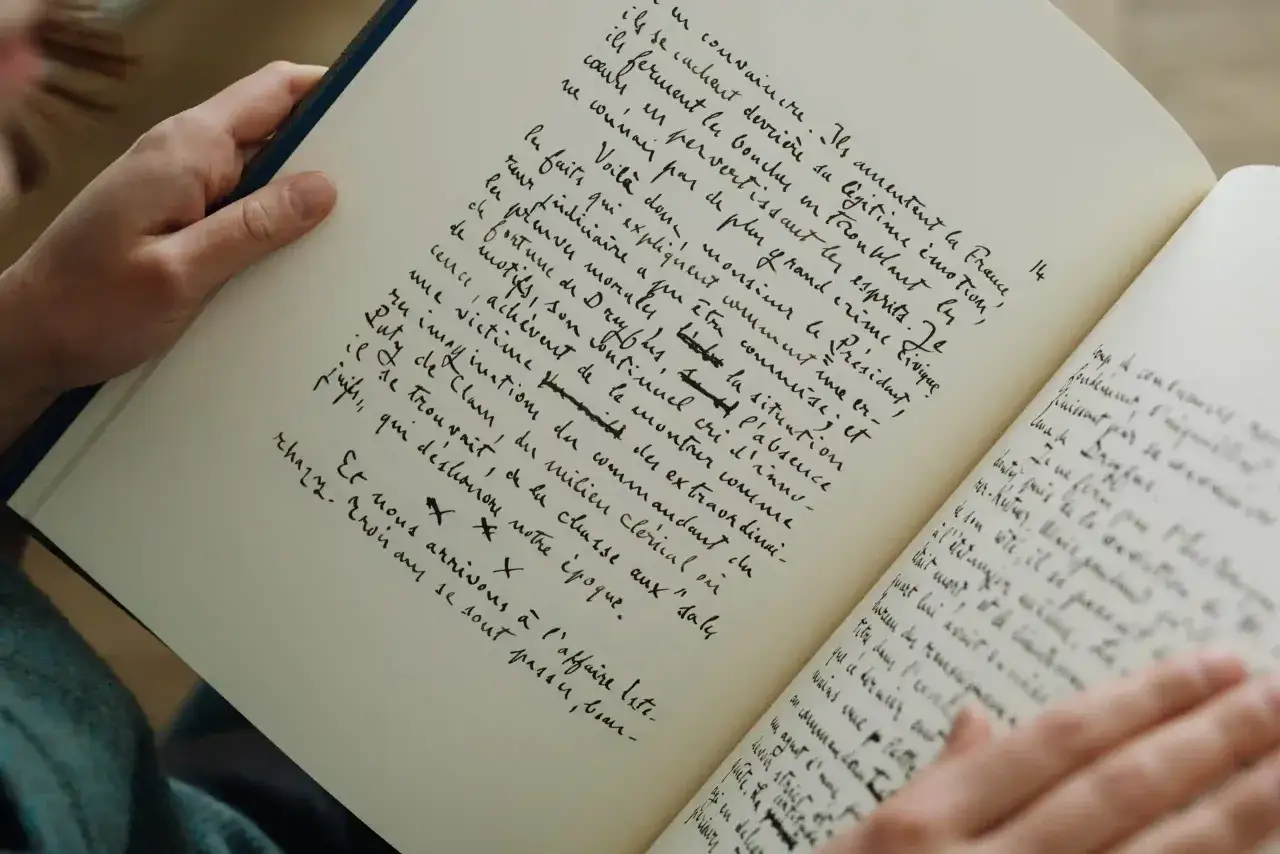 Mains tenant un livre ouvert, pages remplies d'une écriture manuscrite dense. Un aperçu de la ligne éditoriale des éditions Grasset, peut-être un manuscrit inédit.