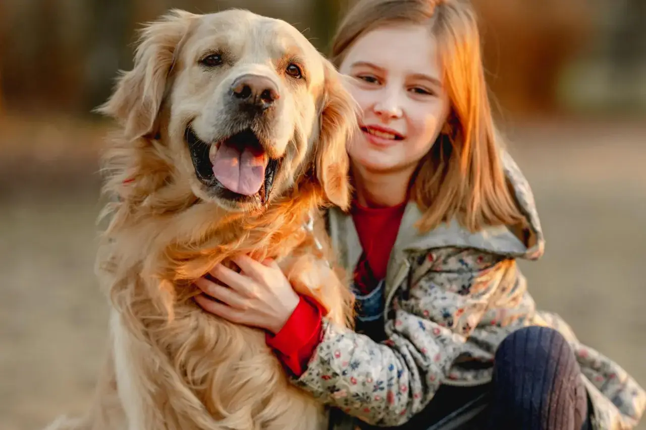 Uśmiechnięta dziewczynka tuli swojego rudego golden retrievera.