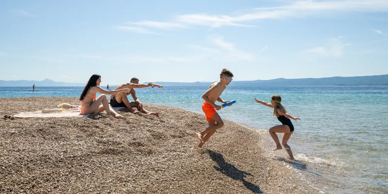 Rodzina na plaży w Chorwacji z dziećmi. Zabawa pistoletami na wodę, idealne wakacje. Chorwacja z dziećmi blog.