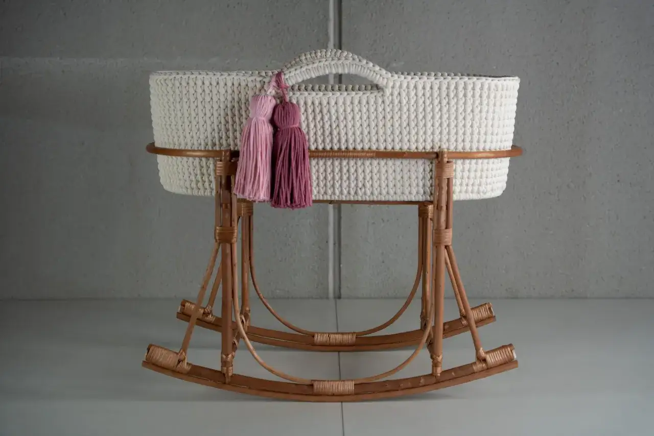 Un dulce moises crochet blanco, con dos borlas rosas, descansa sobre una base de mimbre.