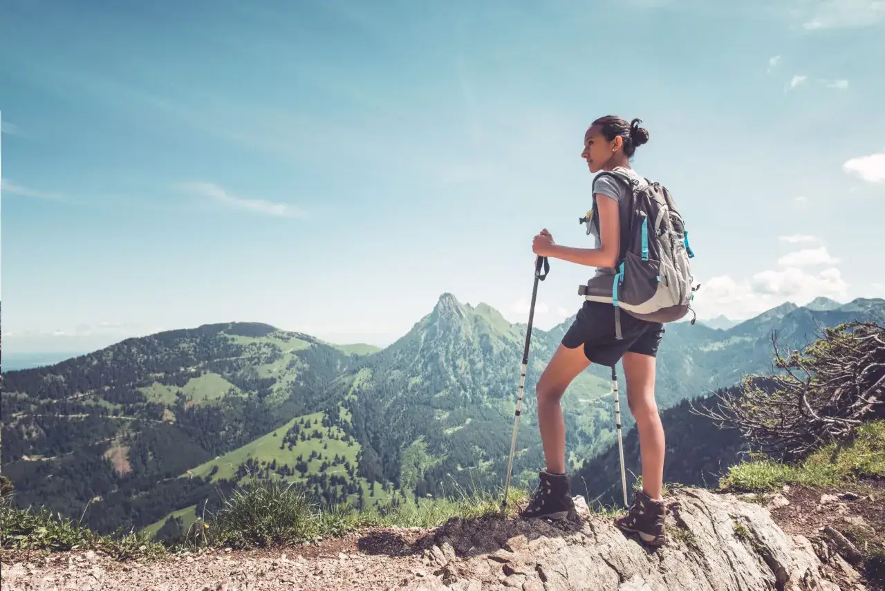 Dziewczyna z plecakiem i kijami trekkingowymi podziwia g&oacute;rski krajobraz.