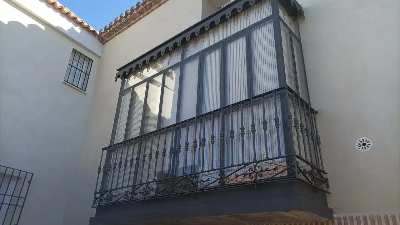 Un elegante ventana mirador con rejas de forja y cortinas transl&uacute;cidas, asom&aacute;ndose a un d&iacute;a soleado.