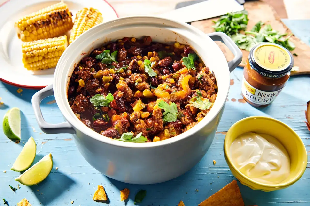 Chili con carne przepis: aromatyczne danie z mięsem, fasolą i kukurydzą, podane z kolendrą, limonką i śmietaną.