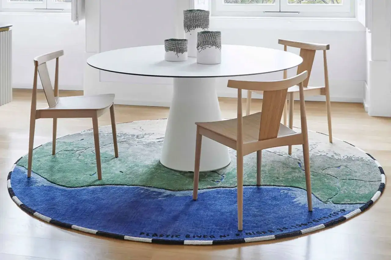 Rund matta under matbord med stolar. Mattan har ett mönster som liknar ett landskap med blått och grönt.