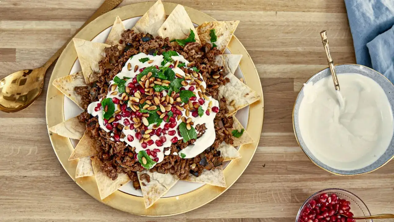 Un plat de fatteh aubergine, garni de viande hachée, de pignons, de grenade et de menthe, servi avec une sauce blanche crémeuse.