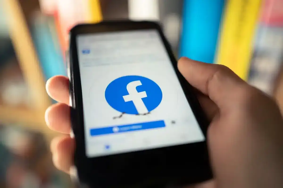 Dłoń trzyma smartfon z logo Facebooka. Dowiedz się, jak usunąć numer telefonu z Facebooka, aby zwiększyć prywatność.