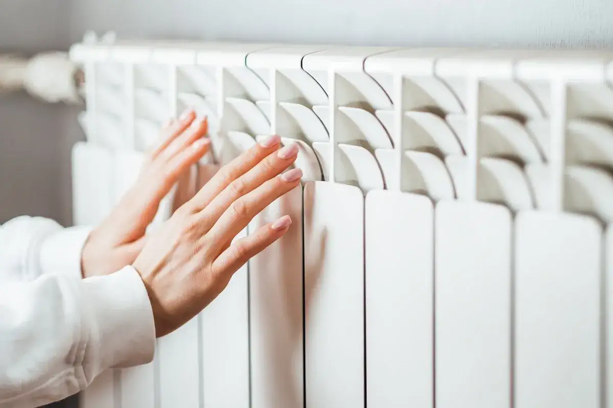 Manos cálidas sobre un convector blanco, sintiendo el calor del hogar.