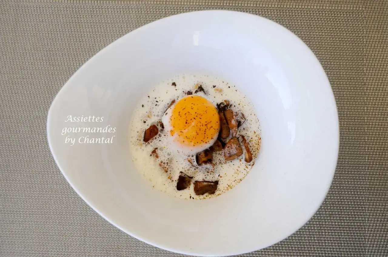 Un œuf poché, entouré de morceaux de champignons et d'une mousse légère, dans une assiette blanche. Des oeufs parfaits pour un repas gourmand.