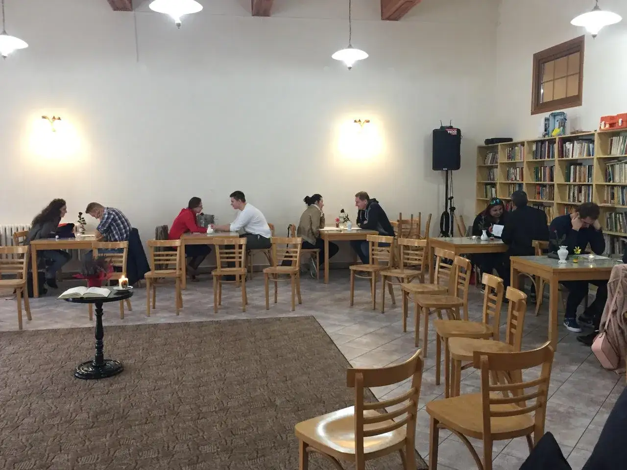 Ludzie siedzą przy stołach, dyskutując. Może to spotkanie dotyczące tego, ile trwają nauki przedmałżeńskie, w przytulnej bibliotece.
