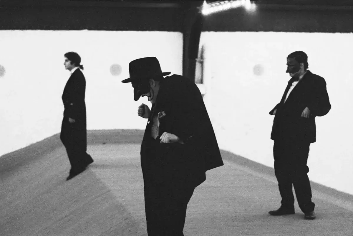 Martine Franck cattura tre figure mascherate in abiti eleganti, un'atmosfera misteriosa e teatrale.