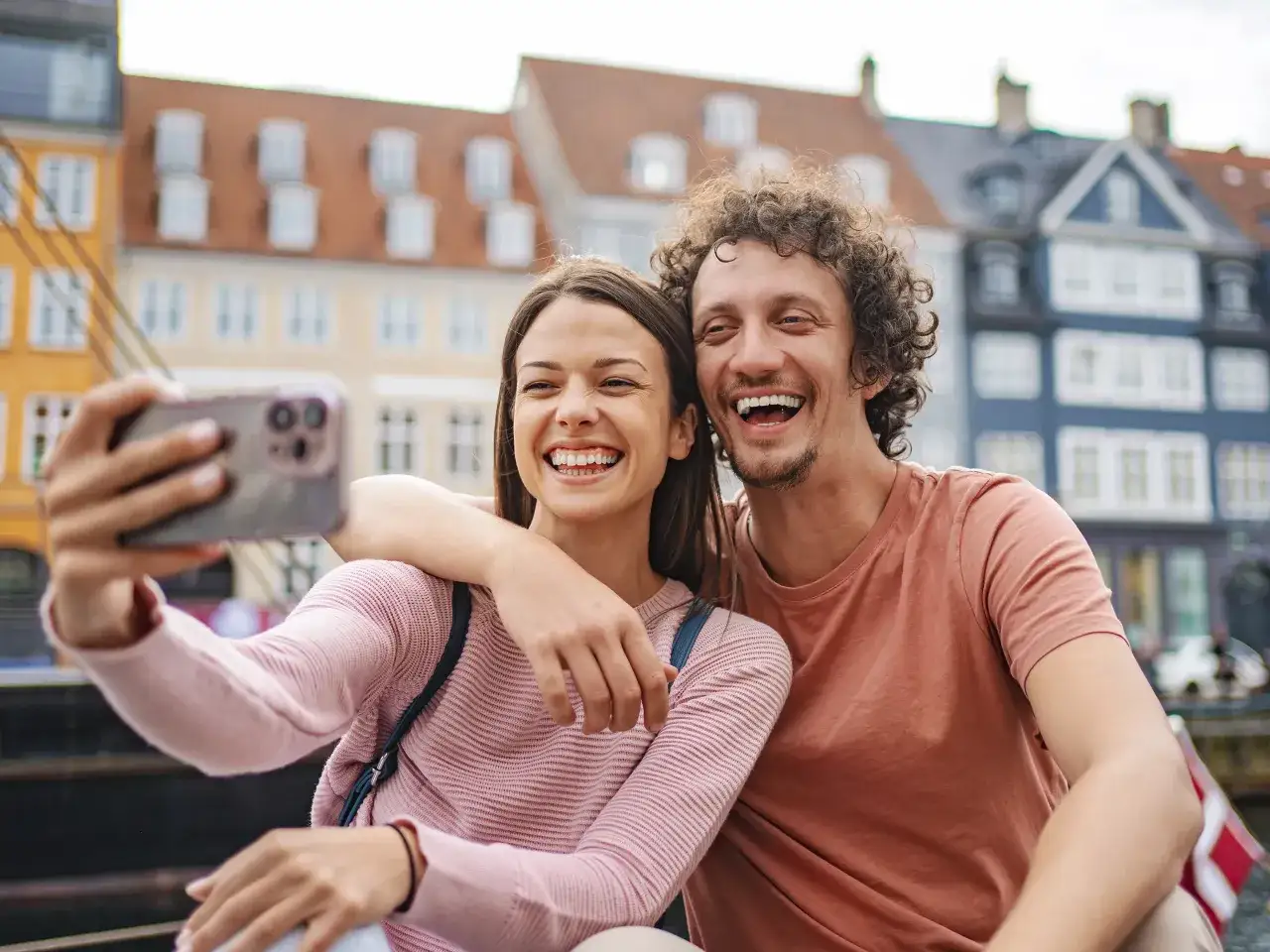Glückliches Paar, das ein Selfie macht, mit verschwommenen bunten Häusern im Hintergrund. Sie sind offensichtlich verliebt und genießen ihre gemeinsame Zeit, was ihren familienstand zusammenlebend unterstreicht.