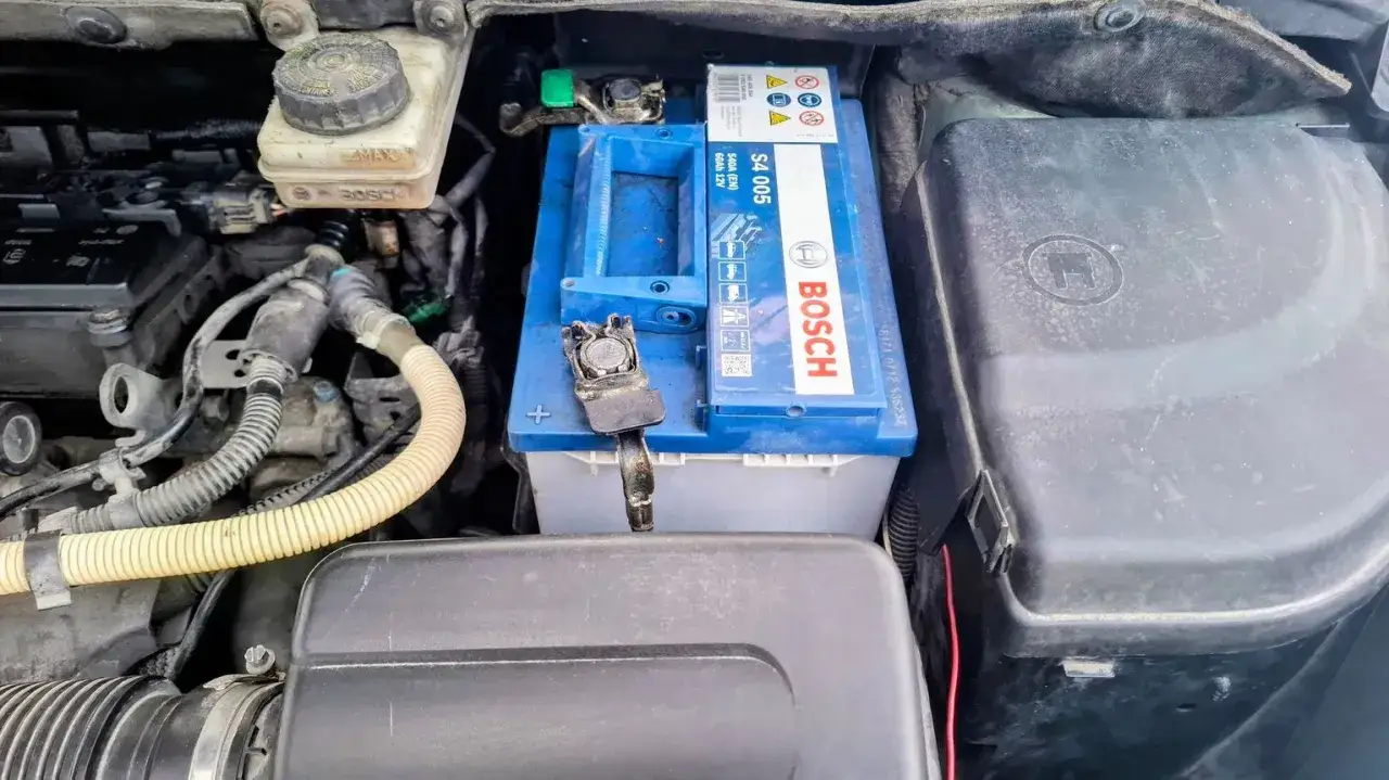 Bilbatteri, Bosch S4 005, redo för kallstart. En bilmekaniker inspekterar batteriet i motorutrymmet.