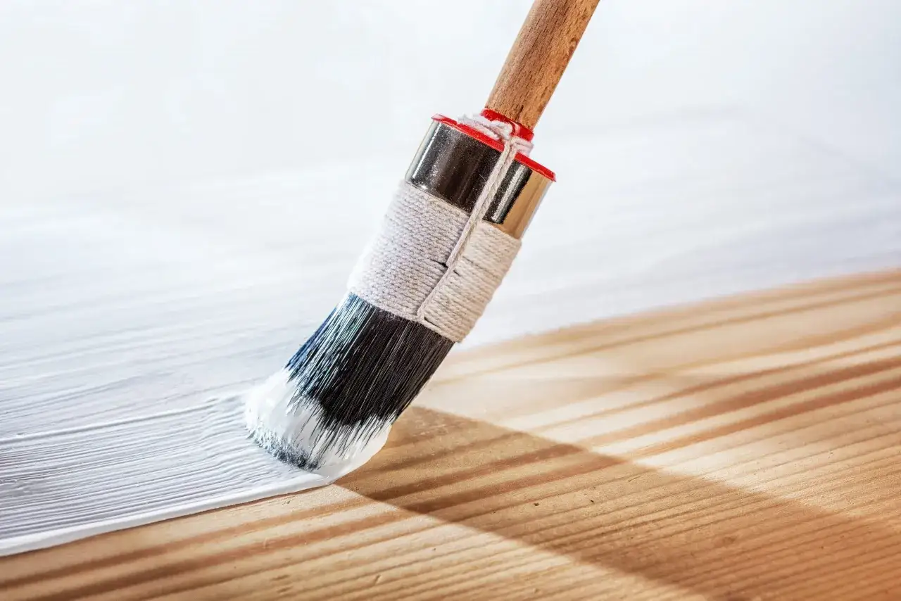 Pennello bianco stende pittura murale su legno grezzo, creando una superficie liscia e luminosa.