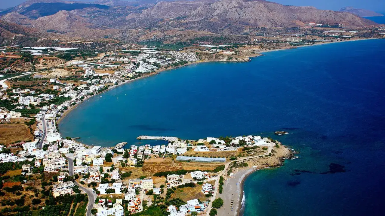 Vacker vy över Makrigialos på Kreta. Vita hus klättrar längs kusten mot det djupblå havet, med berg i bakgrunden.