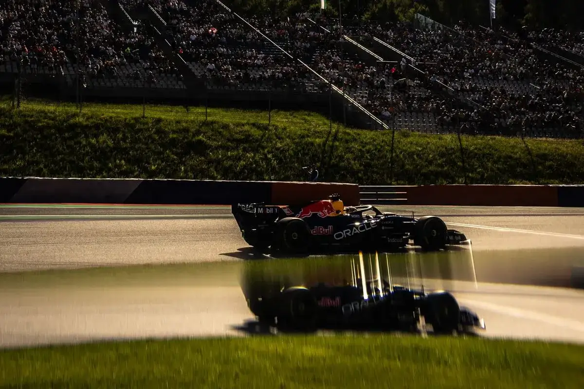 Un coche de Red Bull en la clasificaci&oacute;n F1 Austria, con p&uacute;blico en las gradas y un reflejo en la pista mojada.