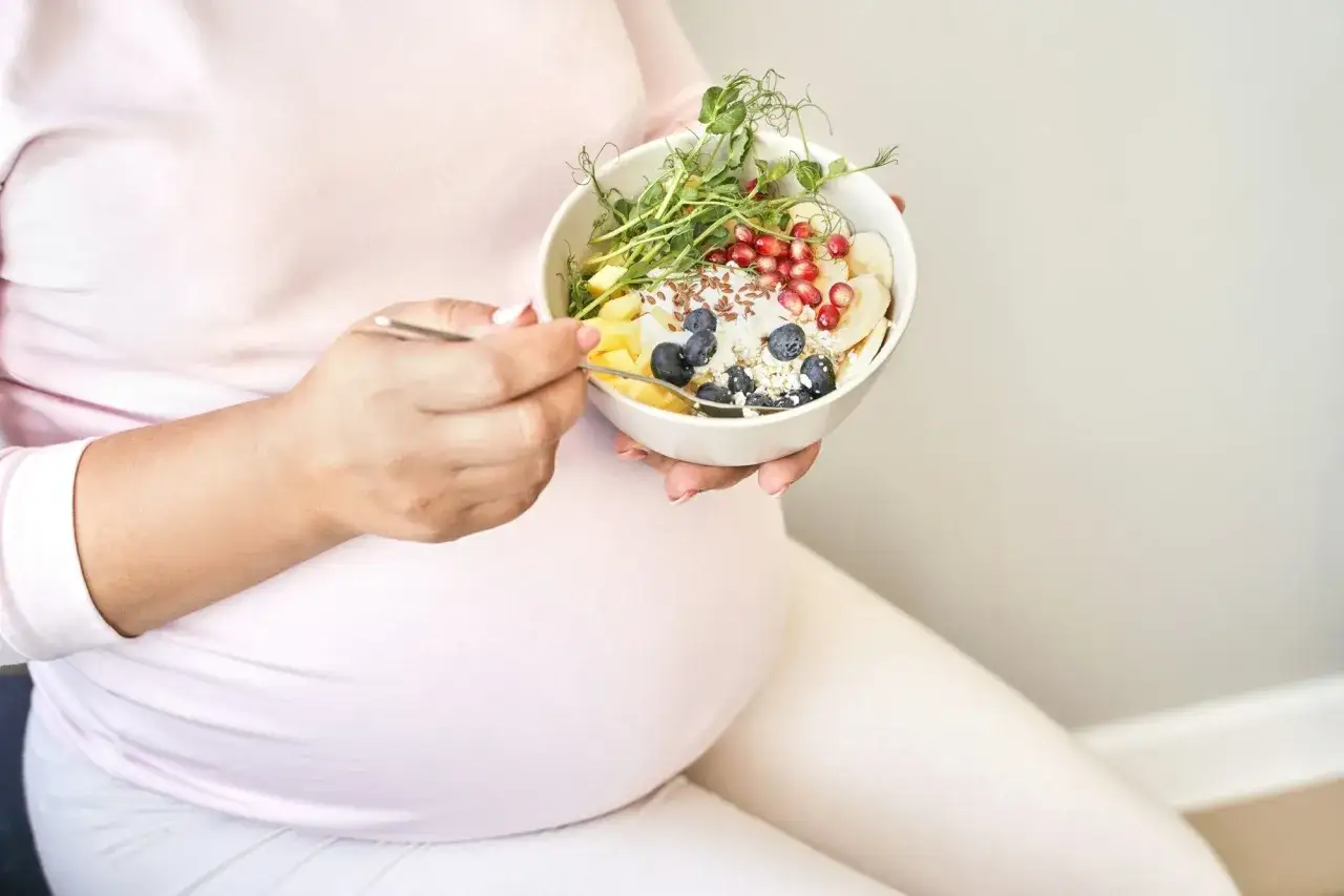 Schwanger mit einer Schüssel voller Obst, Beeren und Sprossen. Gesunde Ernährung während der Schwangerschaft ist wichtig.