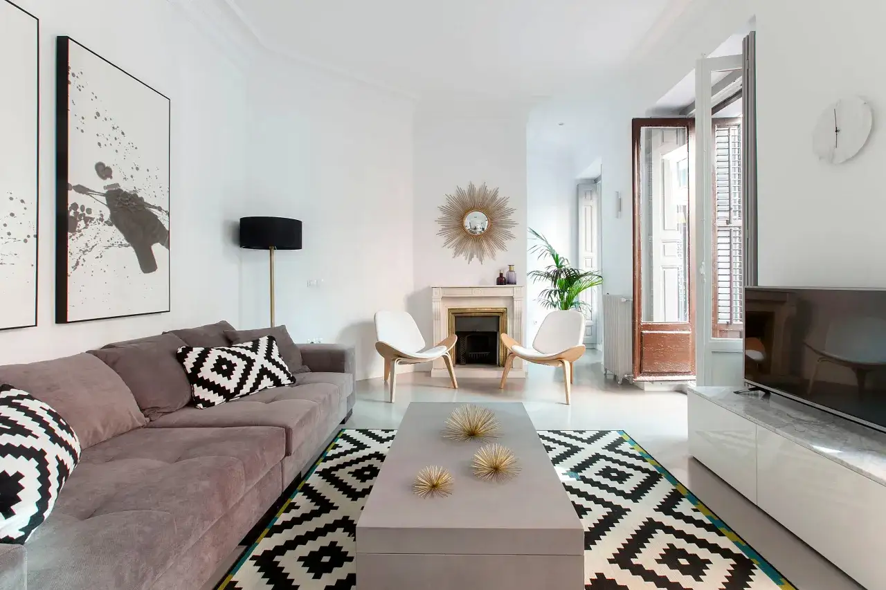 Ideas para decorar un salón rectangular: sofá gris, alfombra geométrica, chimenea, dos sillas blancas y arte abstracto.