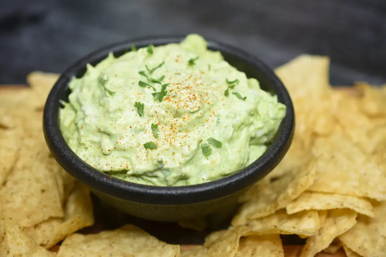 En sk&aring;l med kr&auml;mig guacamole, toppad med persilja och en nypa chilipulver, omgiven av tortillachips. En perfekt kombination av guacamole och cr&egrave;me fraiche.