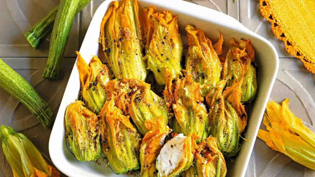 Deliziosi fiori di zucca al forno, ripieni e dorati, pronti per essere gustati. Accanto, zucchine fresche e un tovagliolo giallo.
